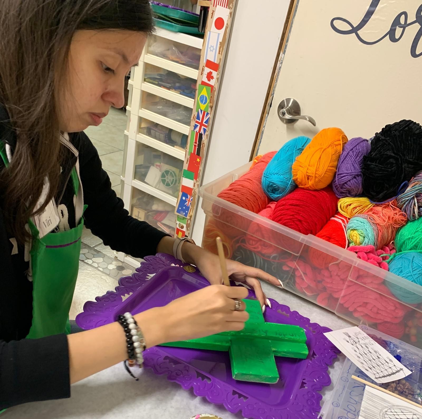 A woman is sitting at a table with a box of yarn in the background