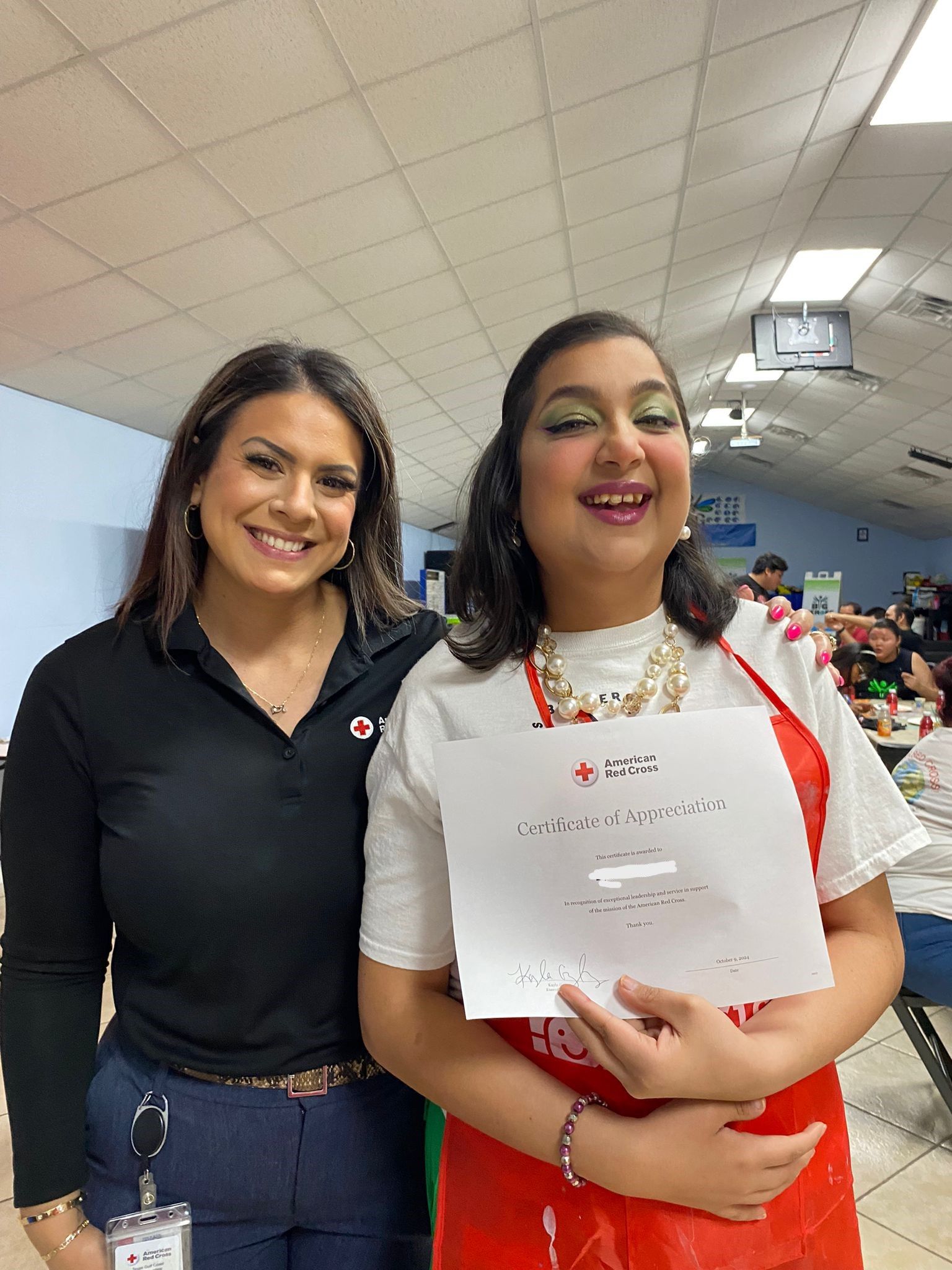 Two women are standing next to each other in a room holding a piece of paper.