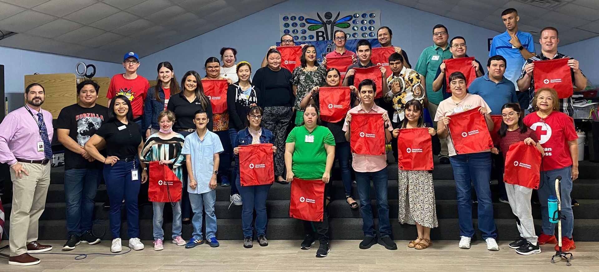 A large group of people are posing for a picture while holding red bags.