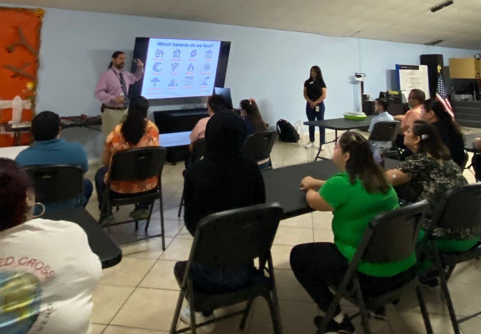 A group of people are sitting at tables in front of a projector screen