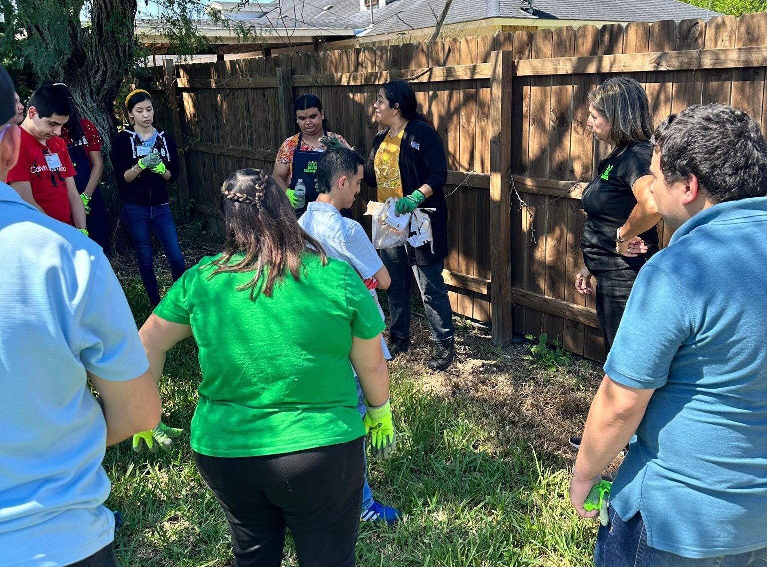 A group of people are standing in a circle in front of a wooden fence.