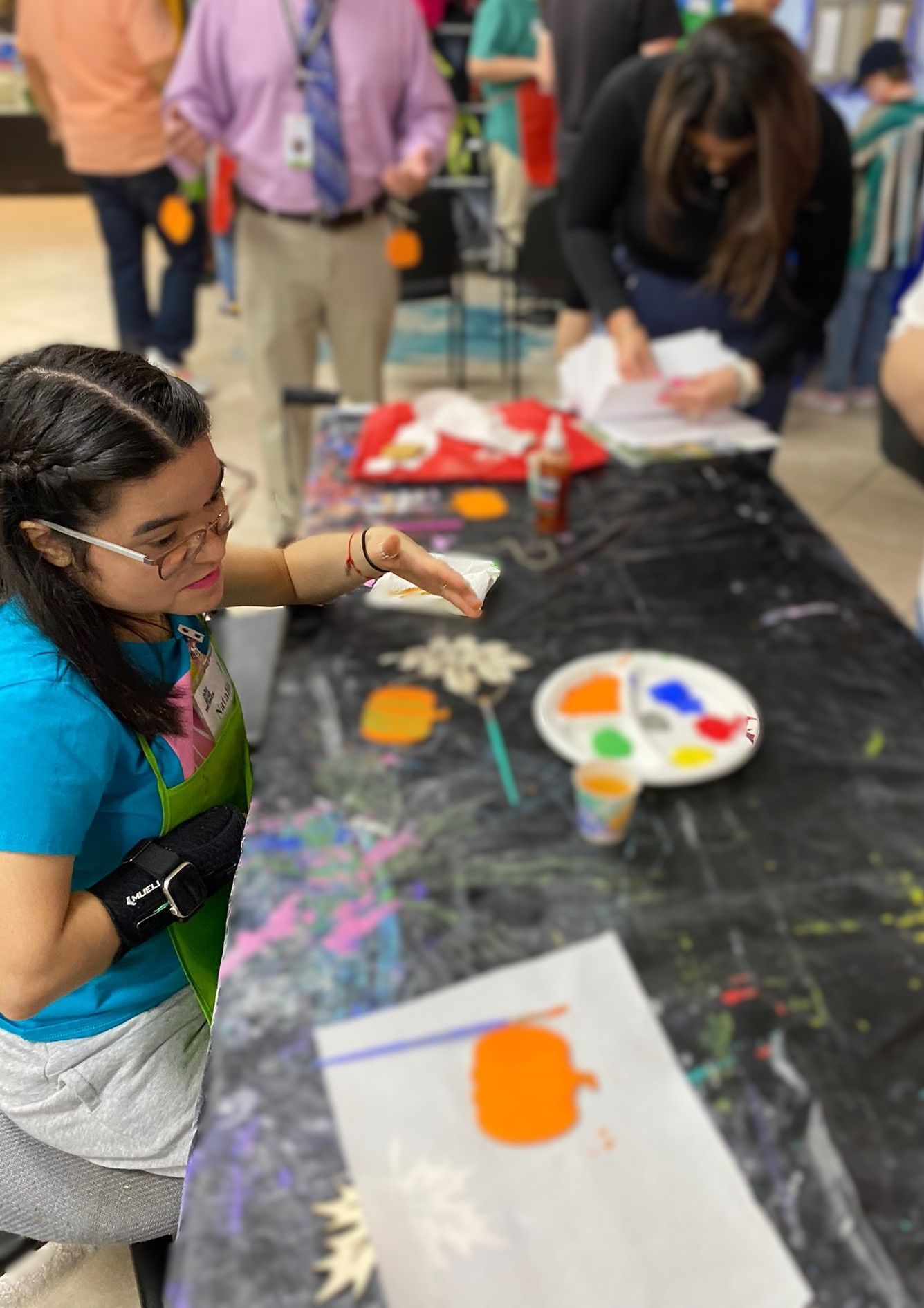 A girl is sitting at a table painting a picture of a pumpkin.