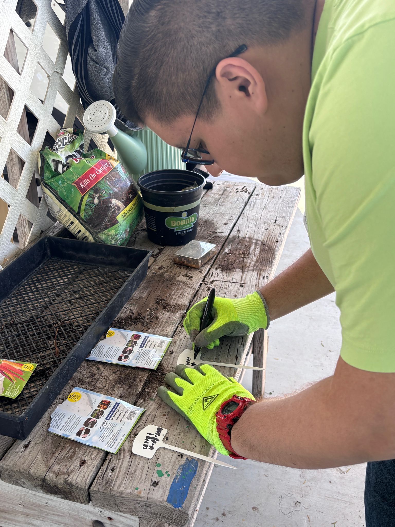 A man wearing yellow gloves is planting seeds on a wooden table.
