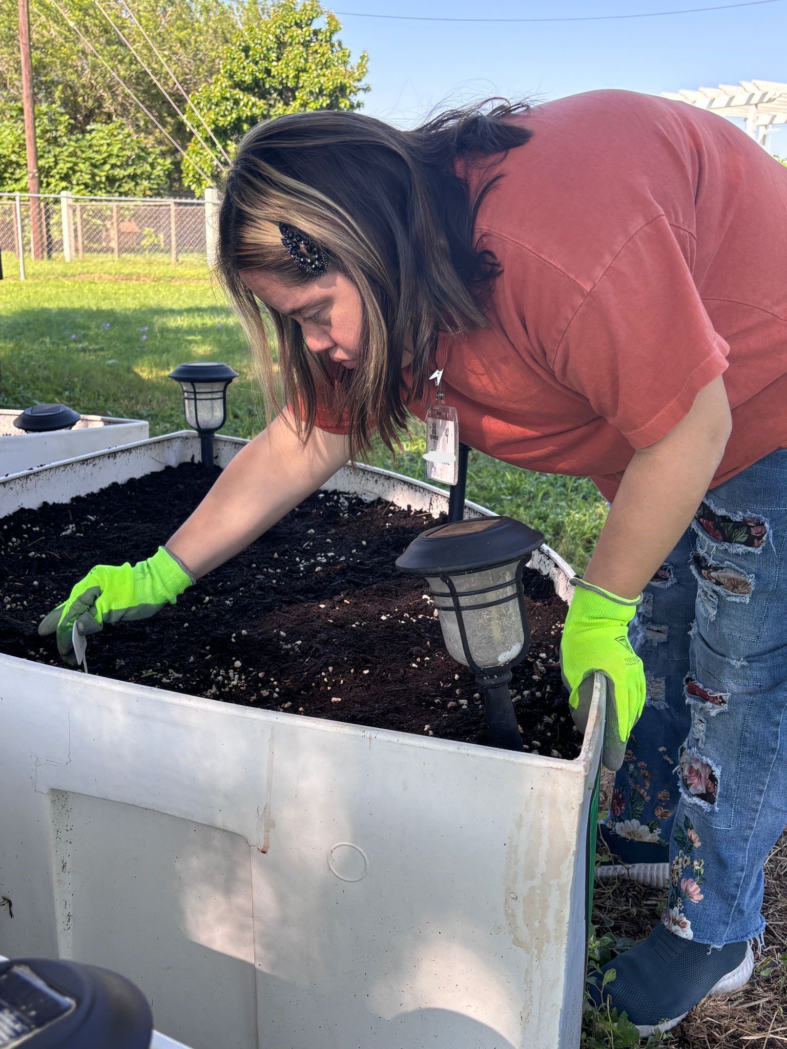 A woman wearing neon green gloves is working in a garden.