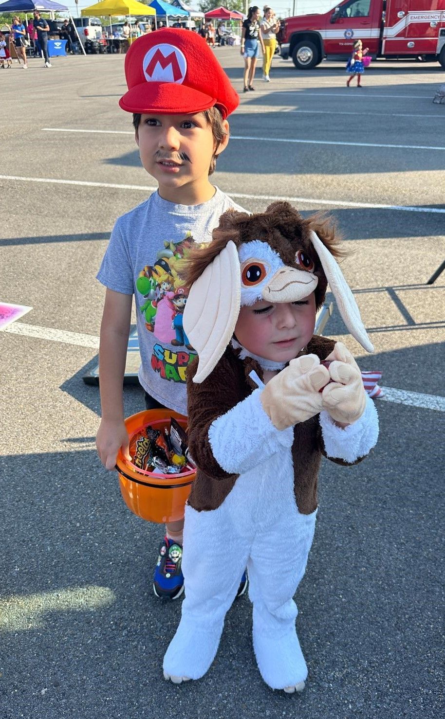 Two young boys dressed in costumes are standing next to each other in a parking lot.