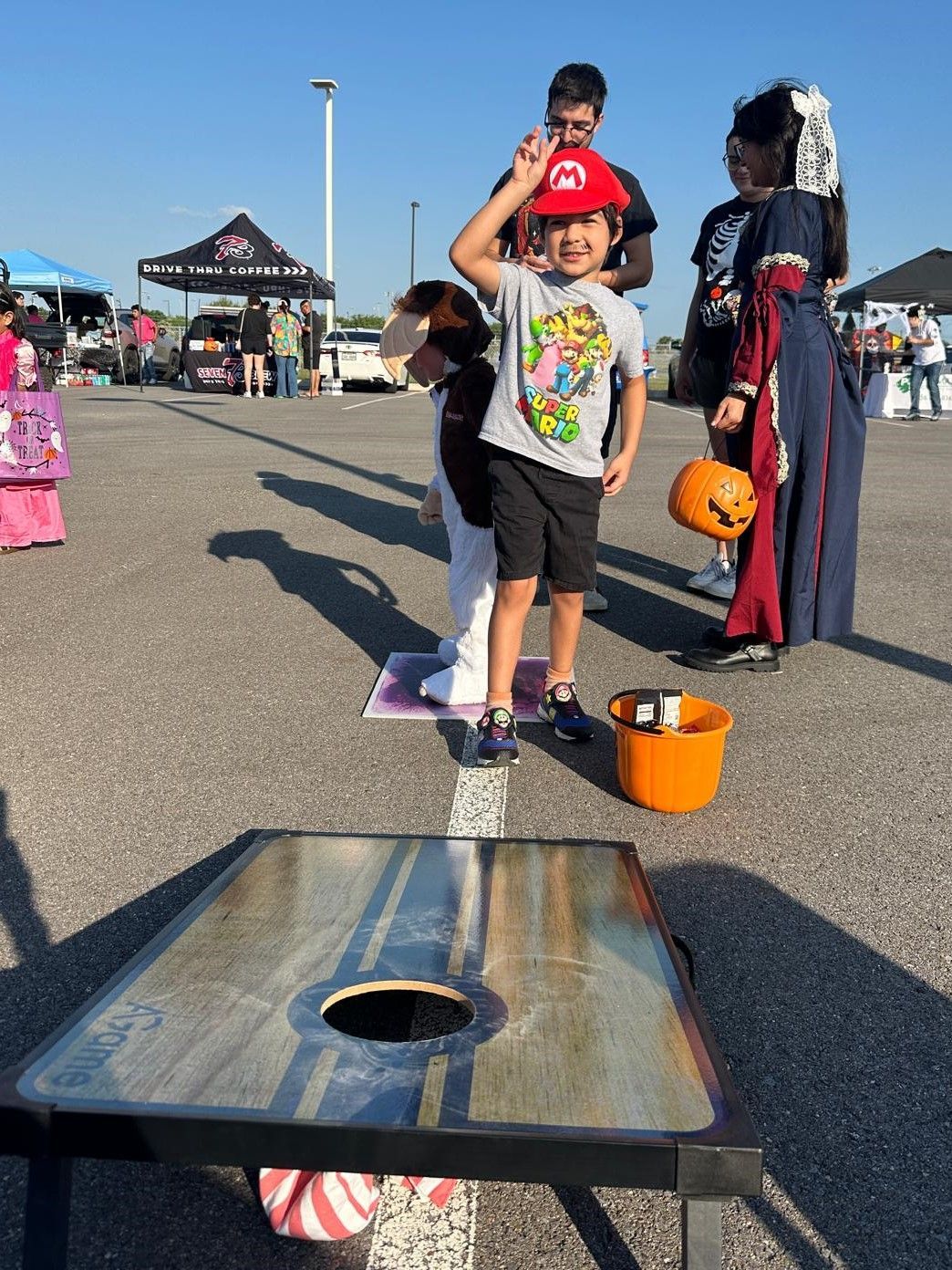 A young boy is playing a game of cornhole in a parking lot.