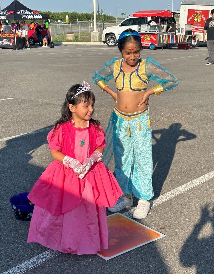 Two little girls dressed in costumes are standing next to each other in a parking lot.
