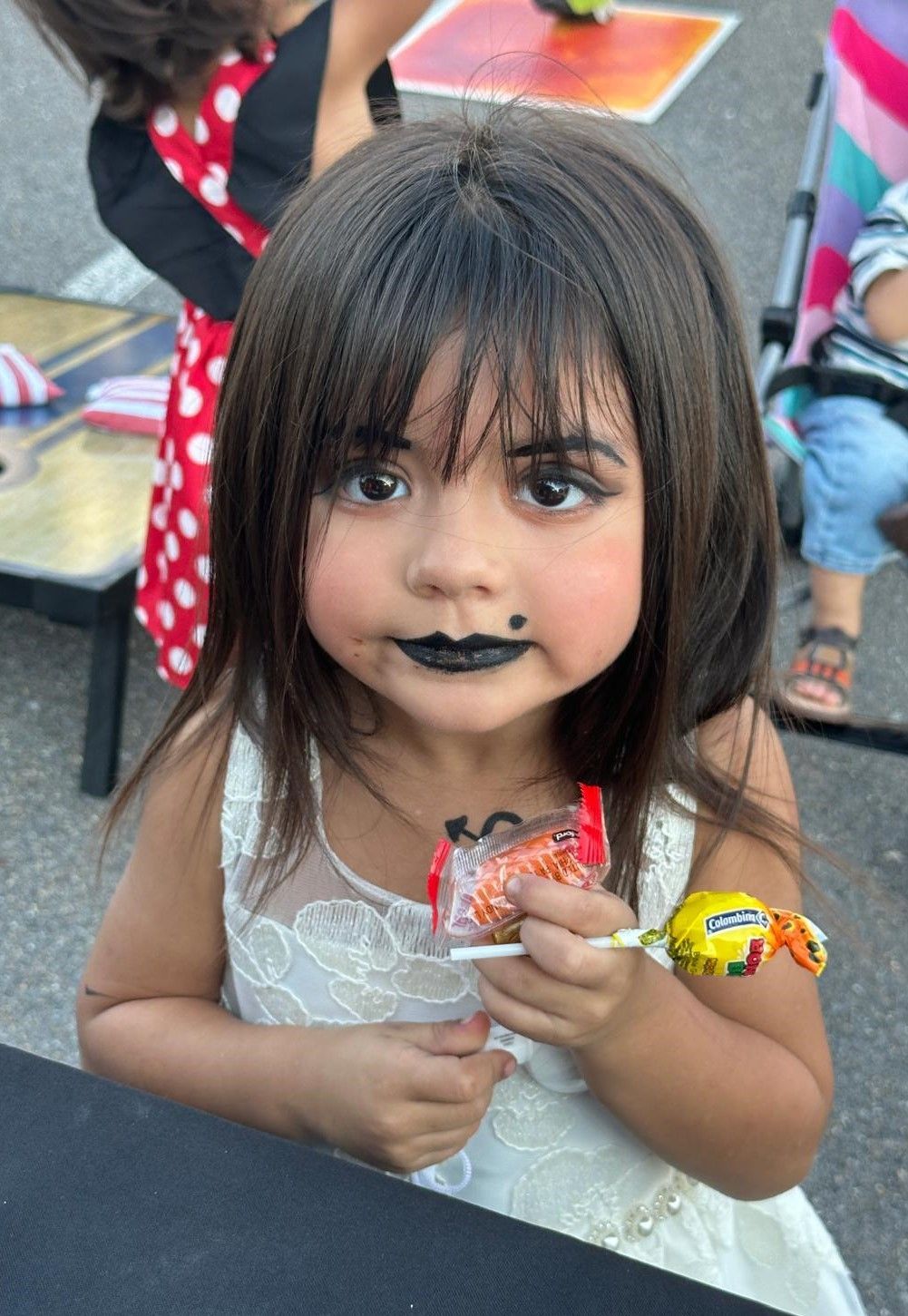 A little girl with black makeup on her face is holding a lollipop.