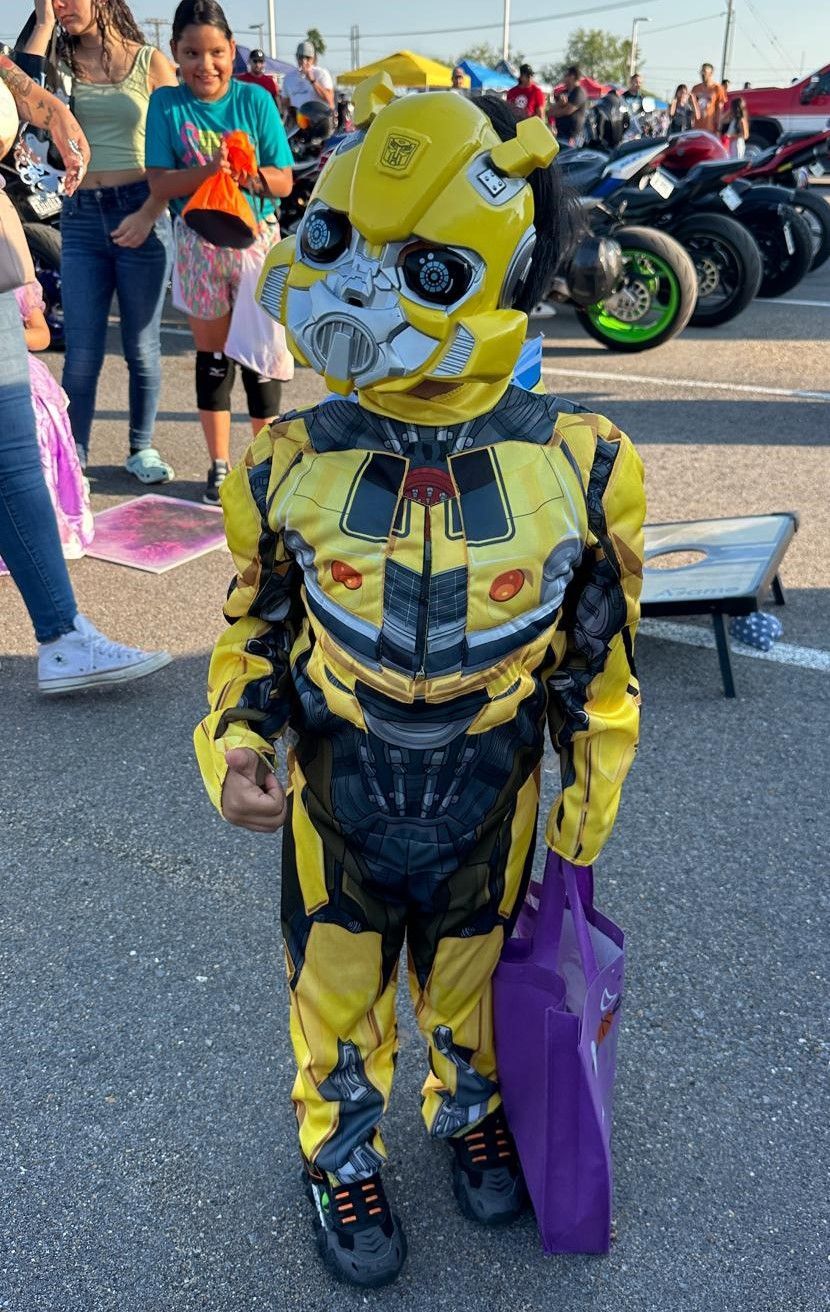 A little boy in a bumblebee costume is standing in a parking lot.
