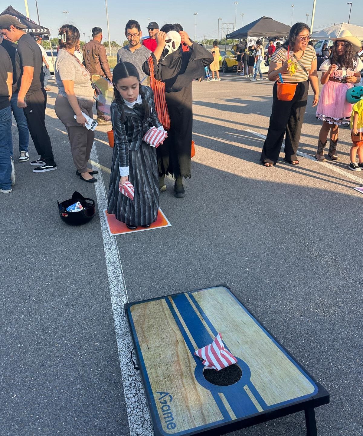 A group of people are playing a game of cornhole in a parking lot.