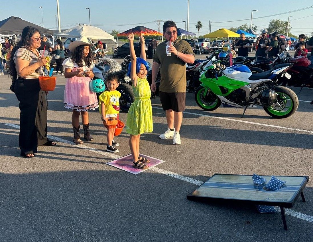 A group of people are standing in a parking lot with motorcycles in the background.
