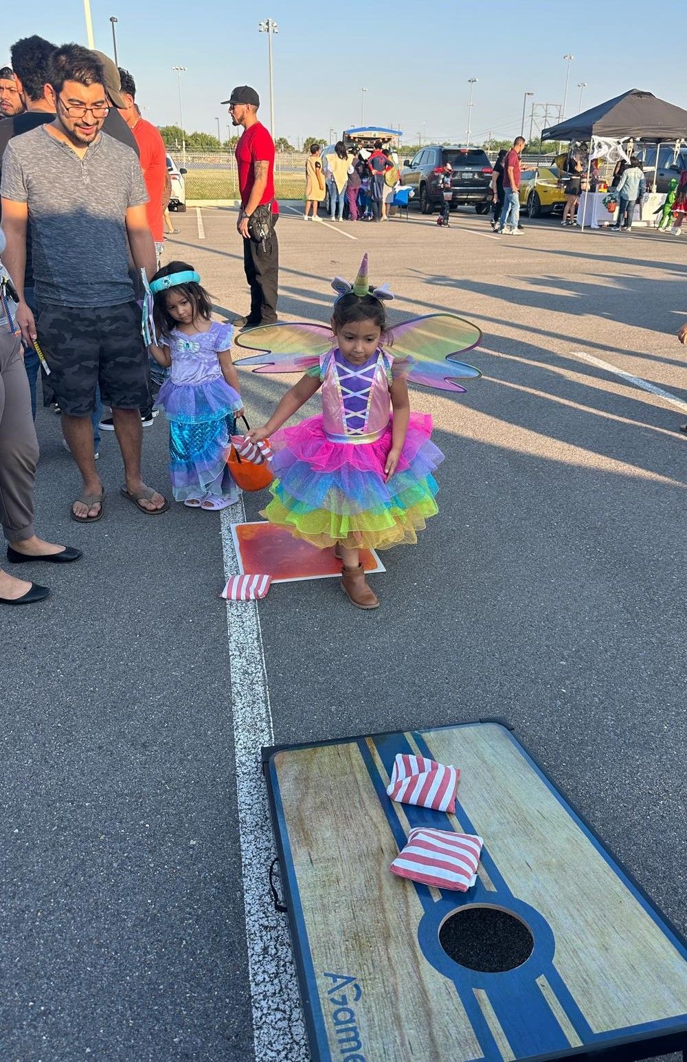 A little girl is playing a game of cornhole in a parking lot.