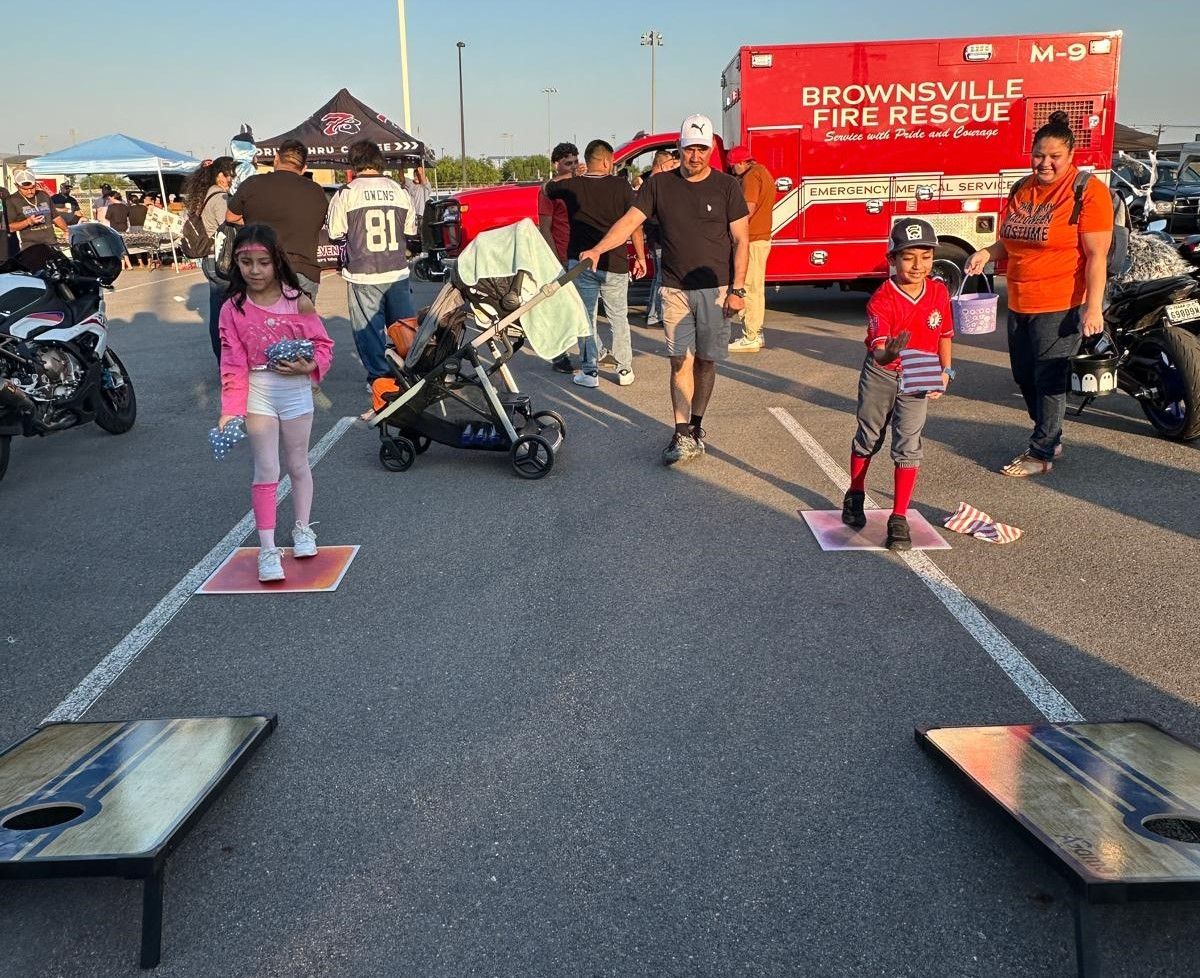 A group of people are playing cornhole in a parking lot in front of a brownsville fire rescue truck.