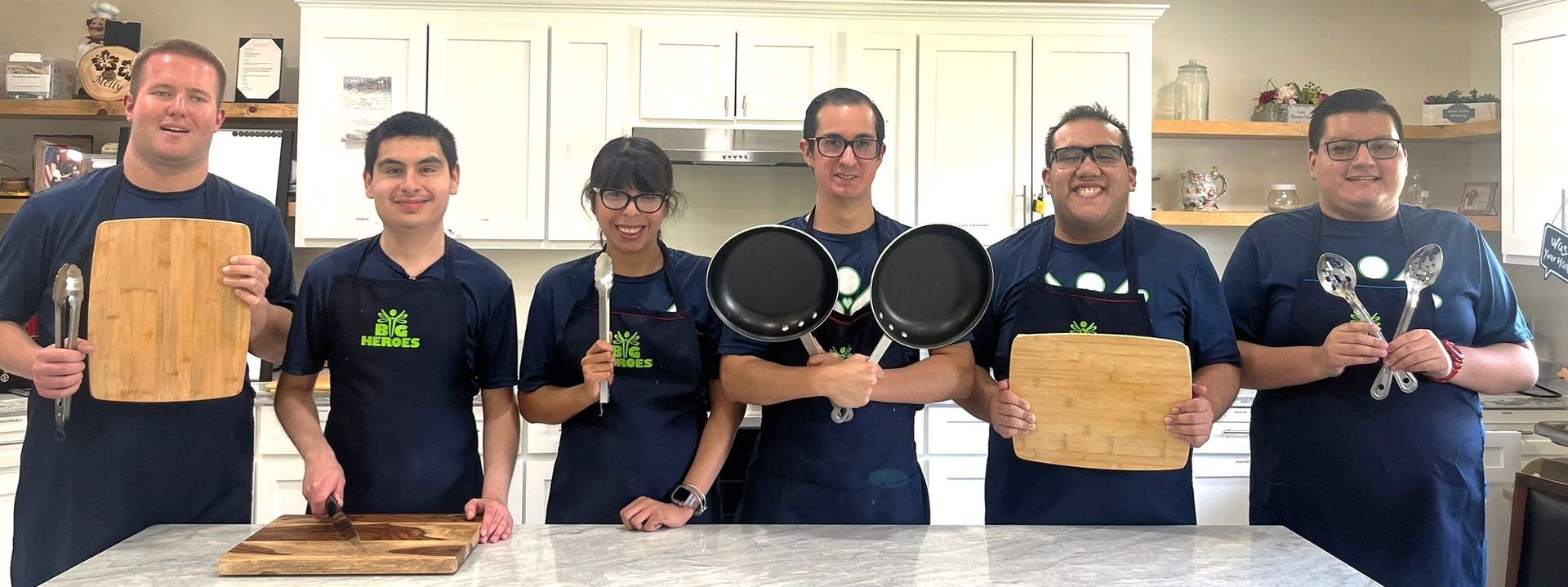 A group of people are standing in a kitchen holding cutting boards and pans.
