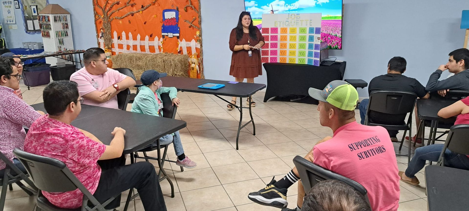 A woman is giving a presentation to a group of people sitting at tables.