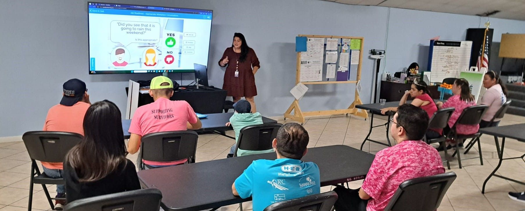 A woman is giving a presentation to a group of people sitting at tables.