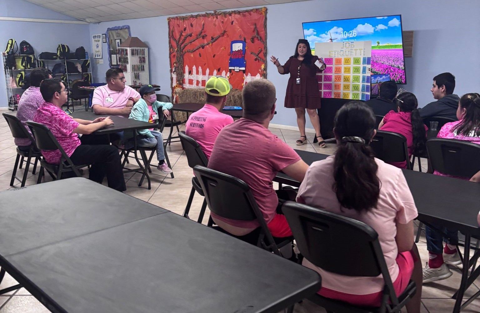 A woman is giving a presentation to a group of people sitting at tables in a room.