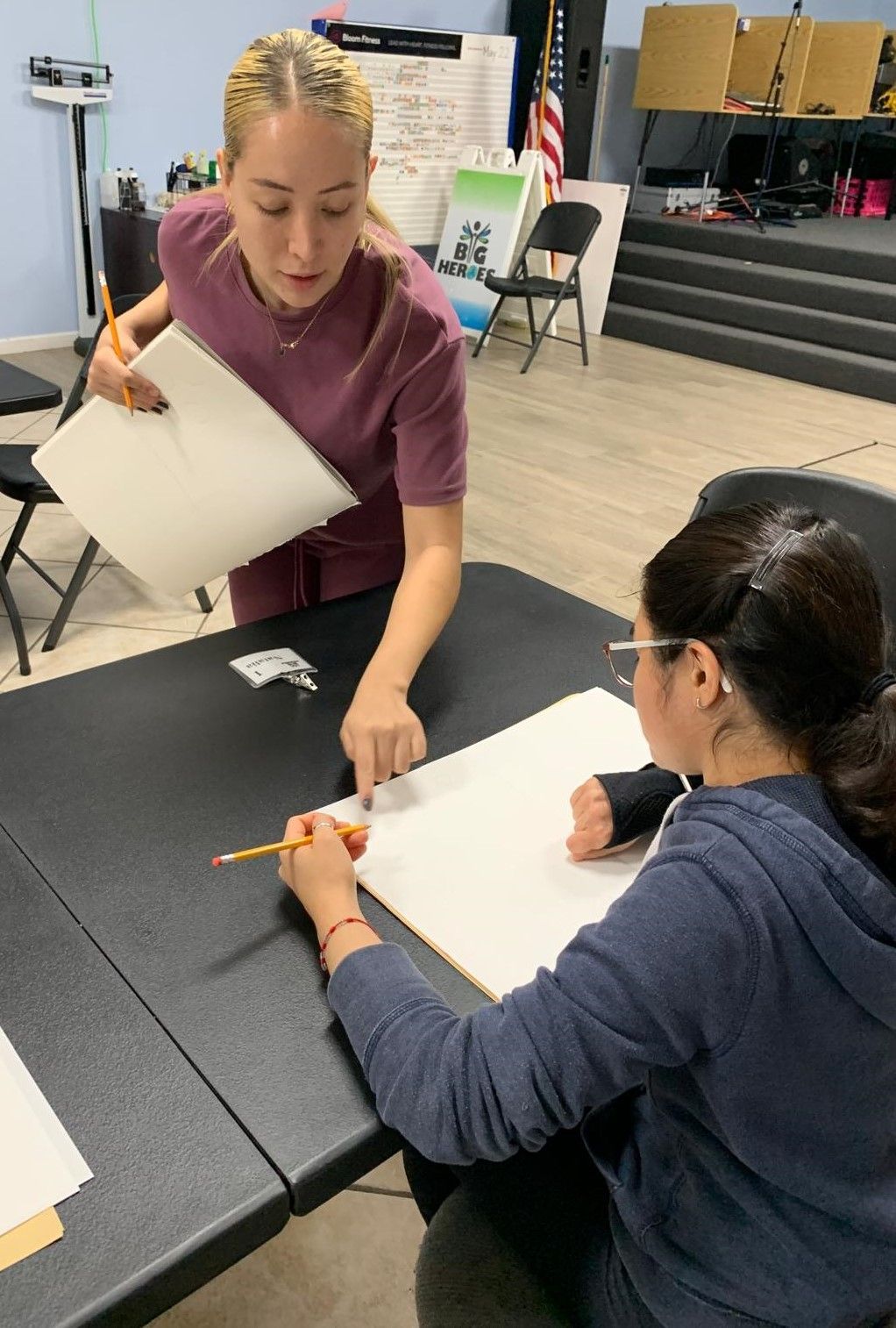 Two women are sitting at a table drawing on a piece of paper.