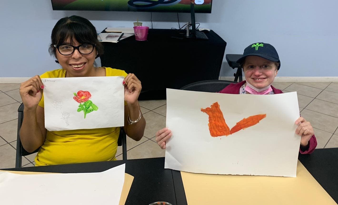 Two women are holding up drawings of a flower and a fox.