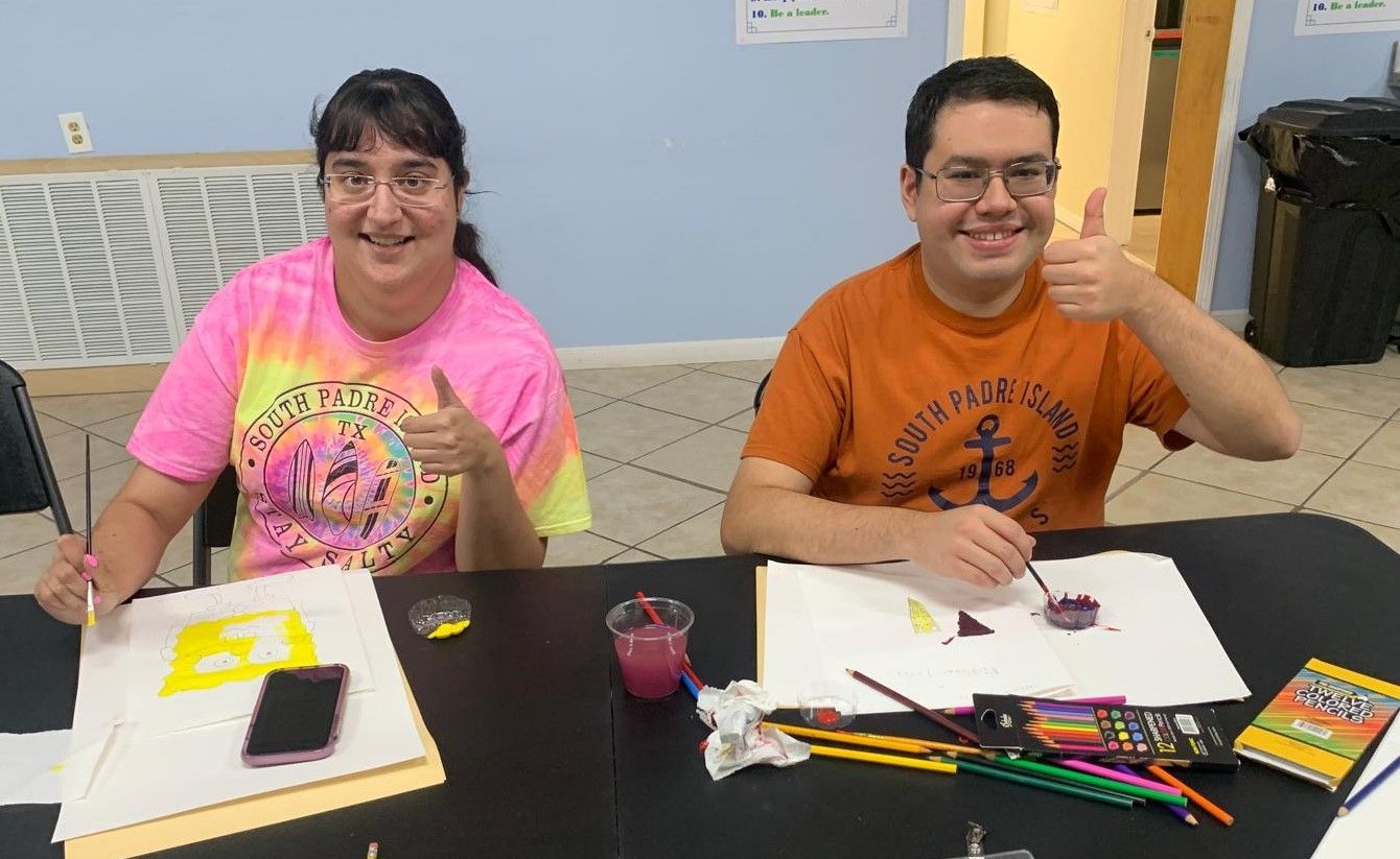 A man and a woman are sitting at a table giving a thumbs up
