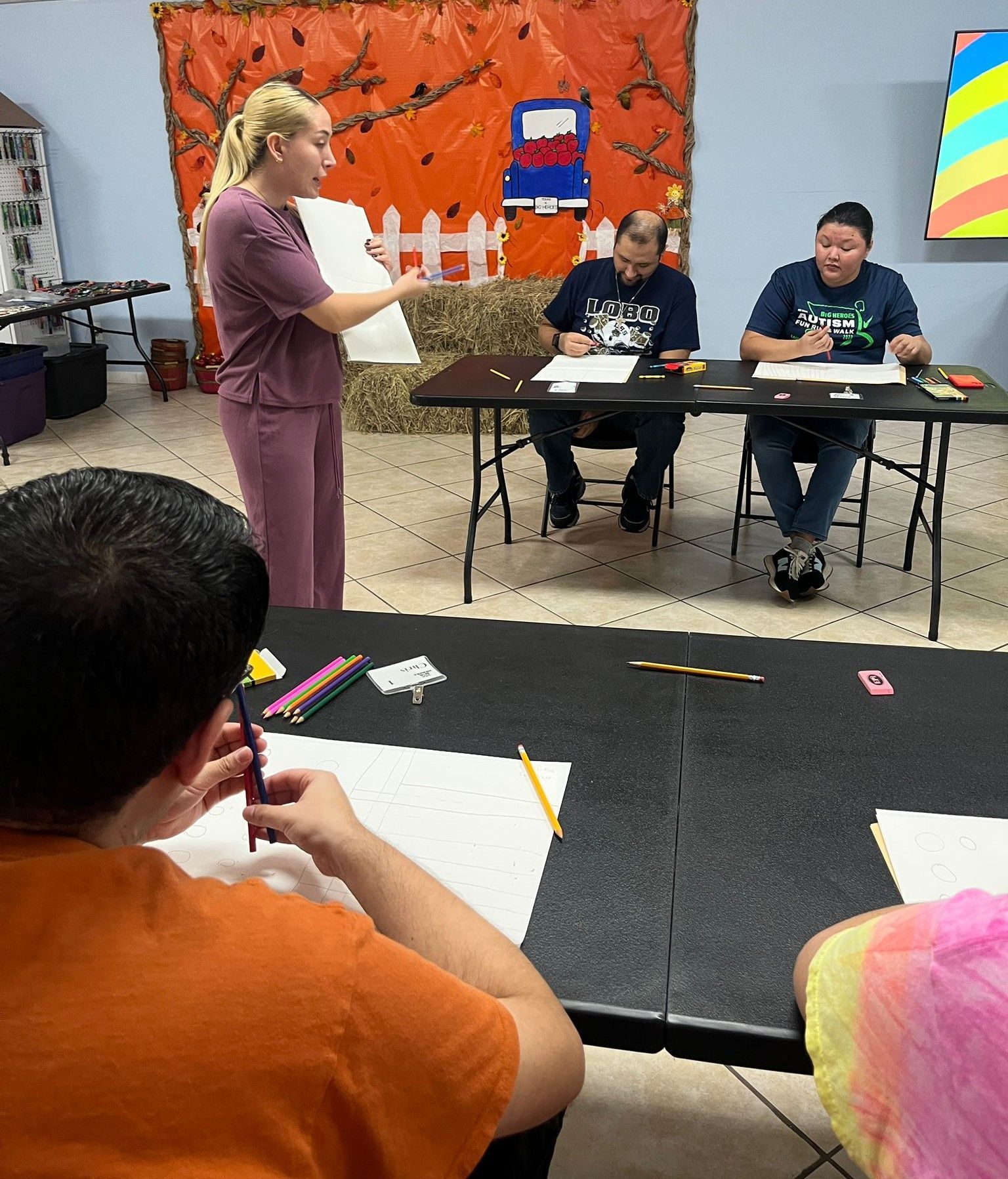 A woman in scrubs is standing in front of a group of people sitting at tables