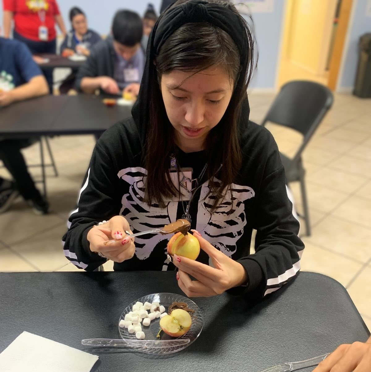 A woman in a skeleton sweatshirt is sitting at a table with a plate of food