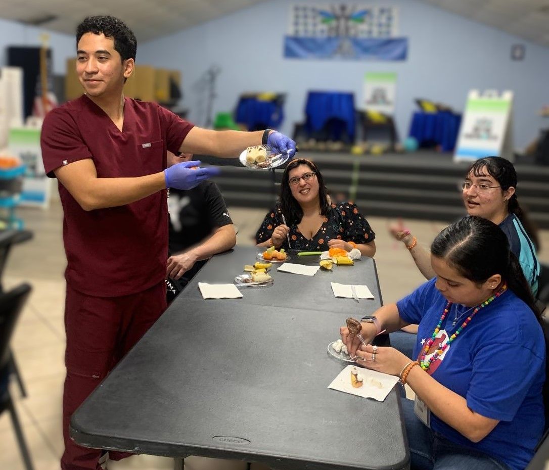 A man in scrubs is serving food to a group of people at a table