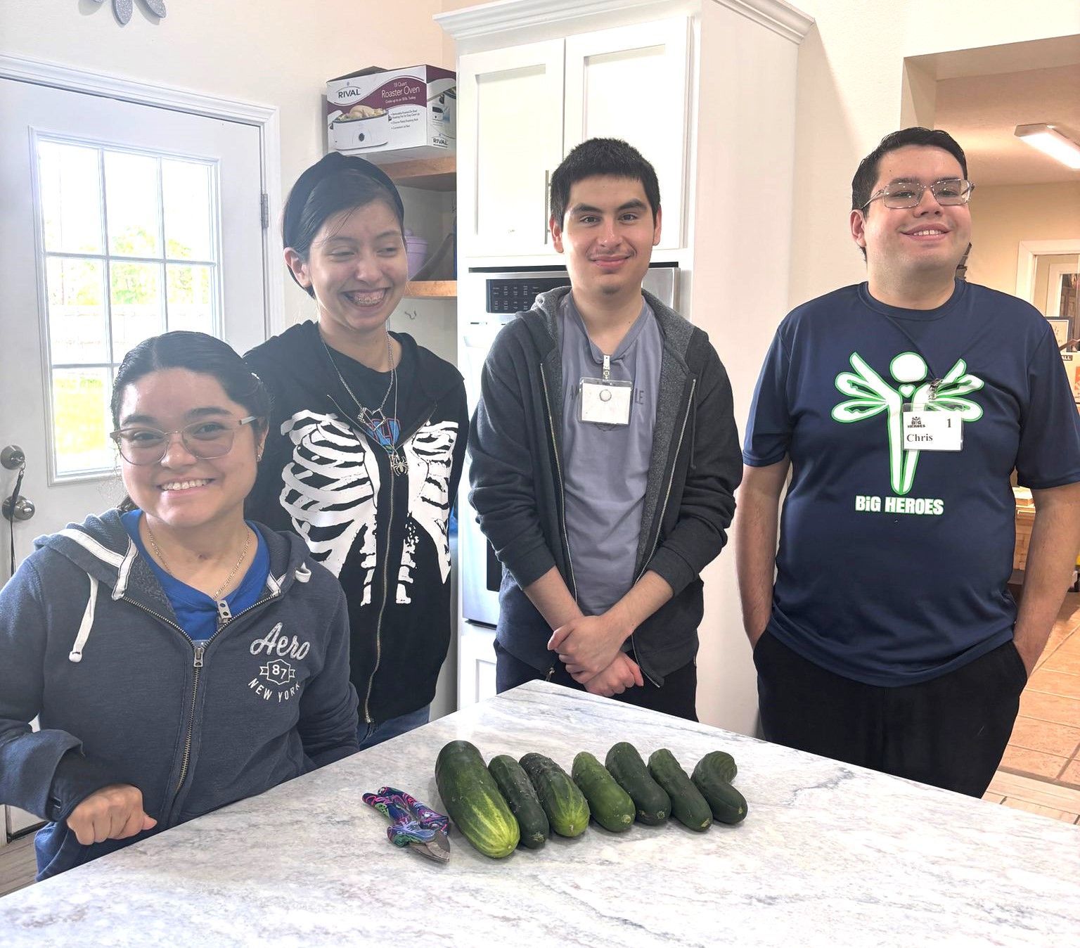 A group of people standing around a counter with cucumbers on it