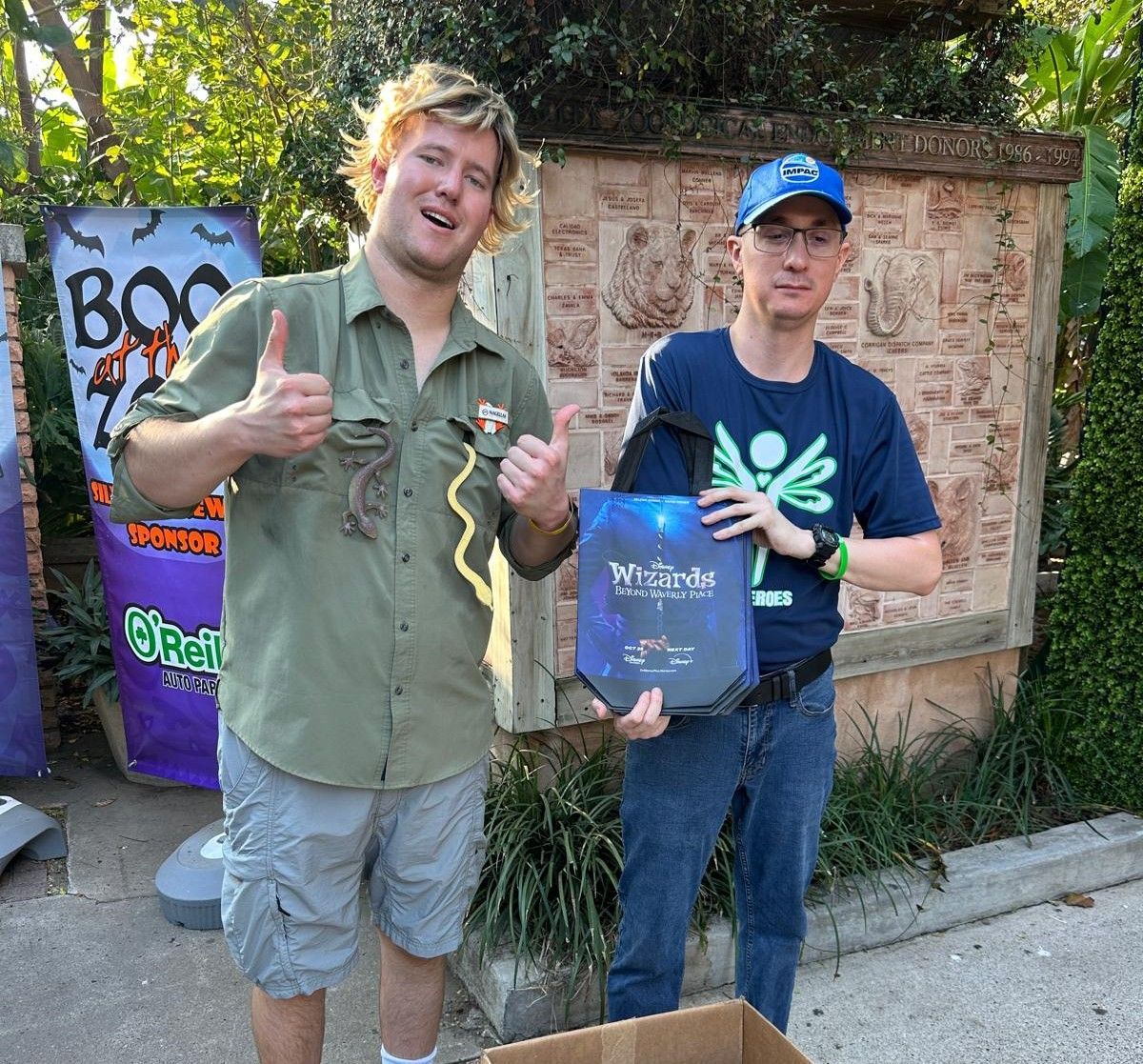 Two men standing next to each other in front of a sign that says boo