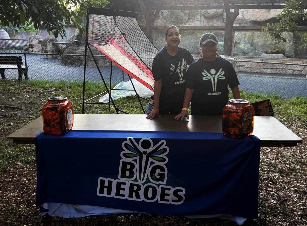 Two people standing behind a table that says big heroes