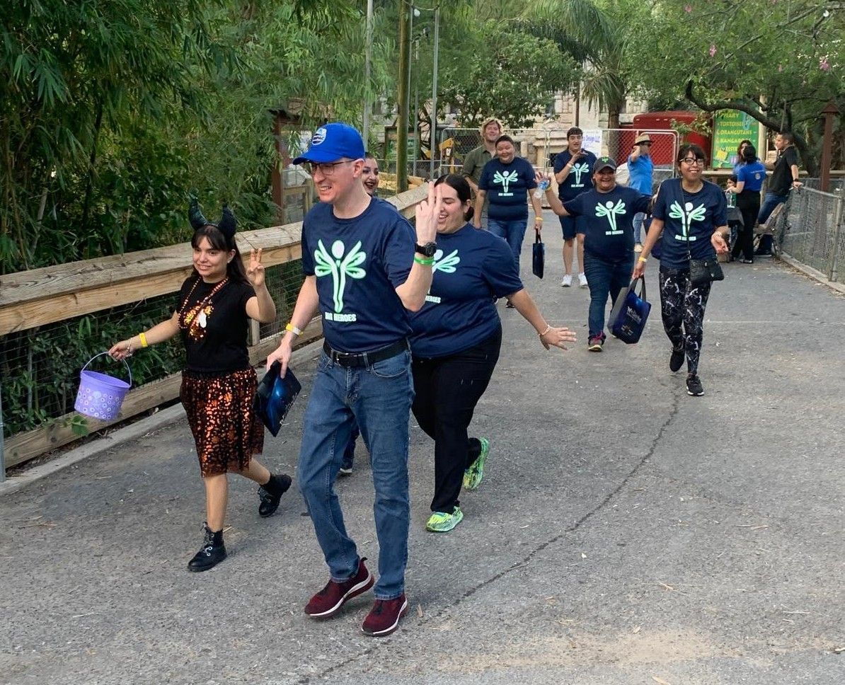 A group of people wearing blue shirts with a tree on them are walking down a street.