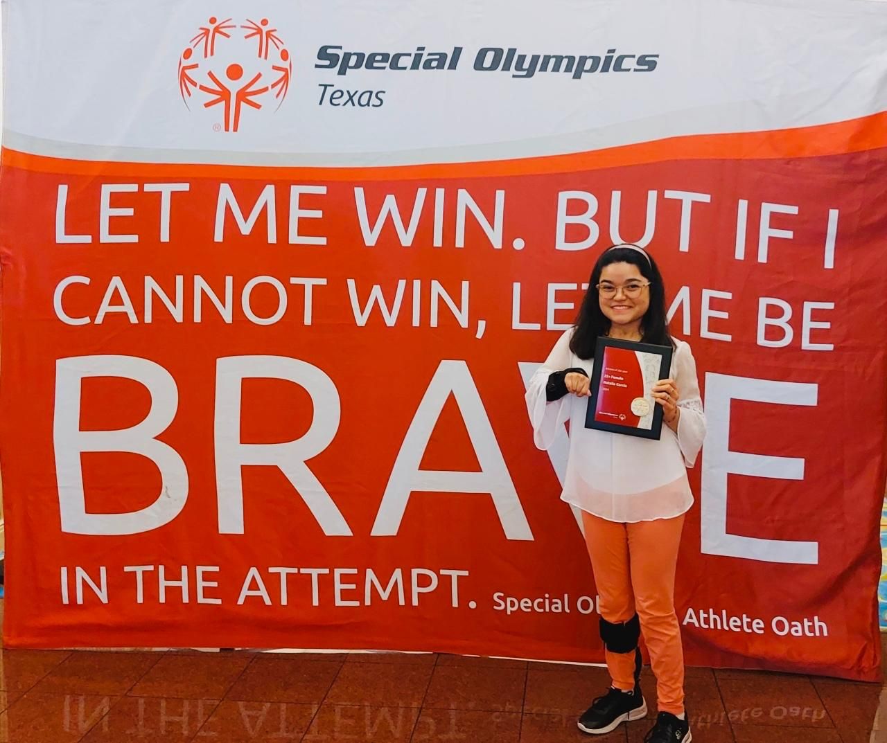 A girl is standing in front of a sign that says let me win but if i cannot win let me be brave in the attempt