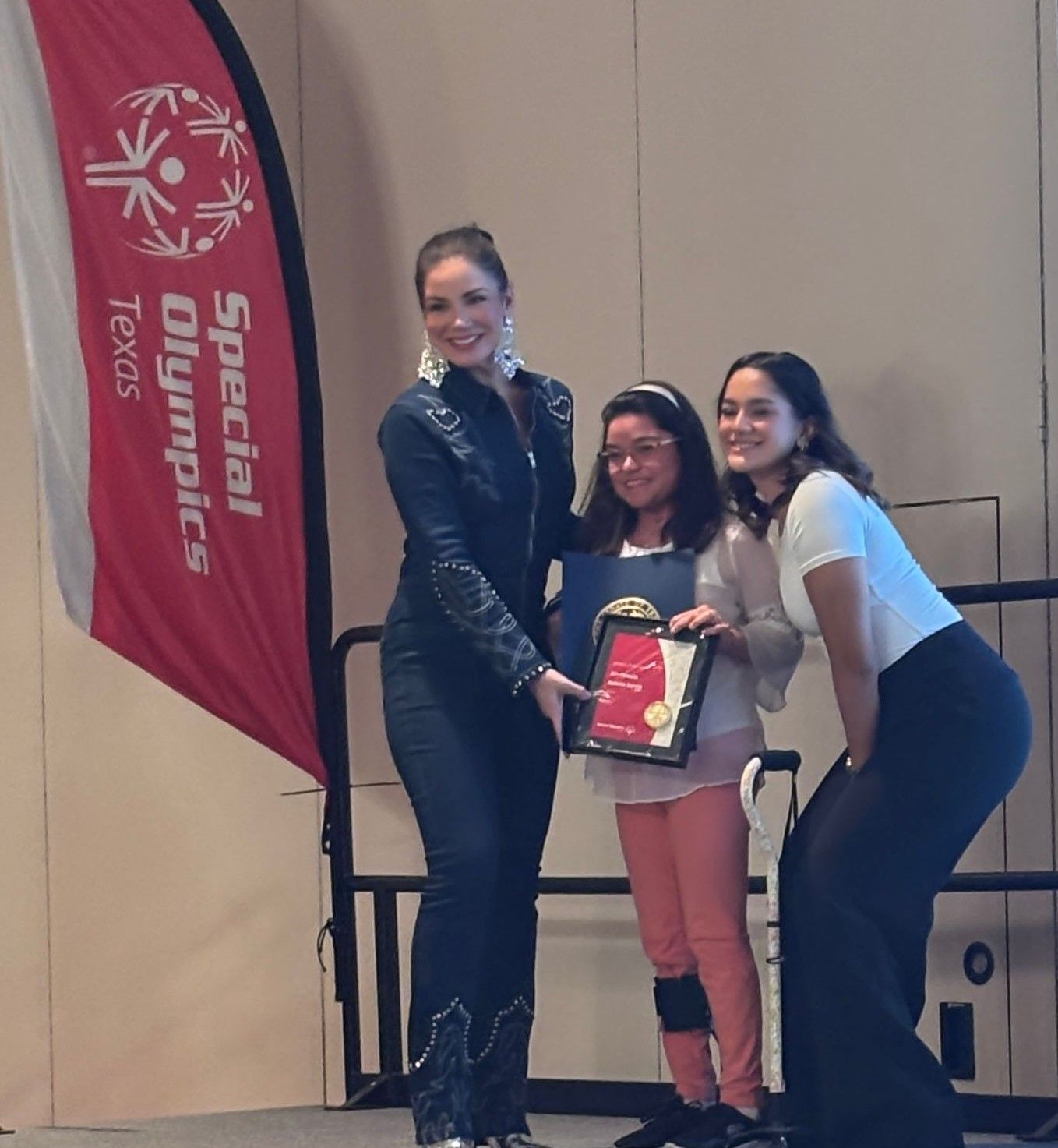 Three women stand in front of a special olympics flag