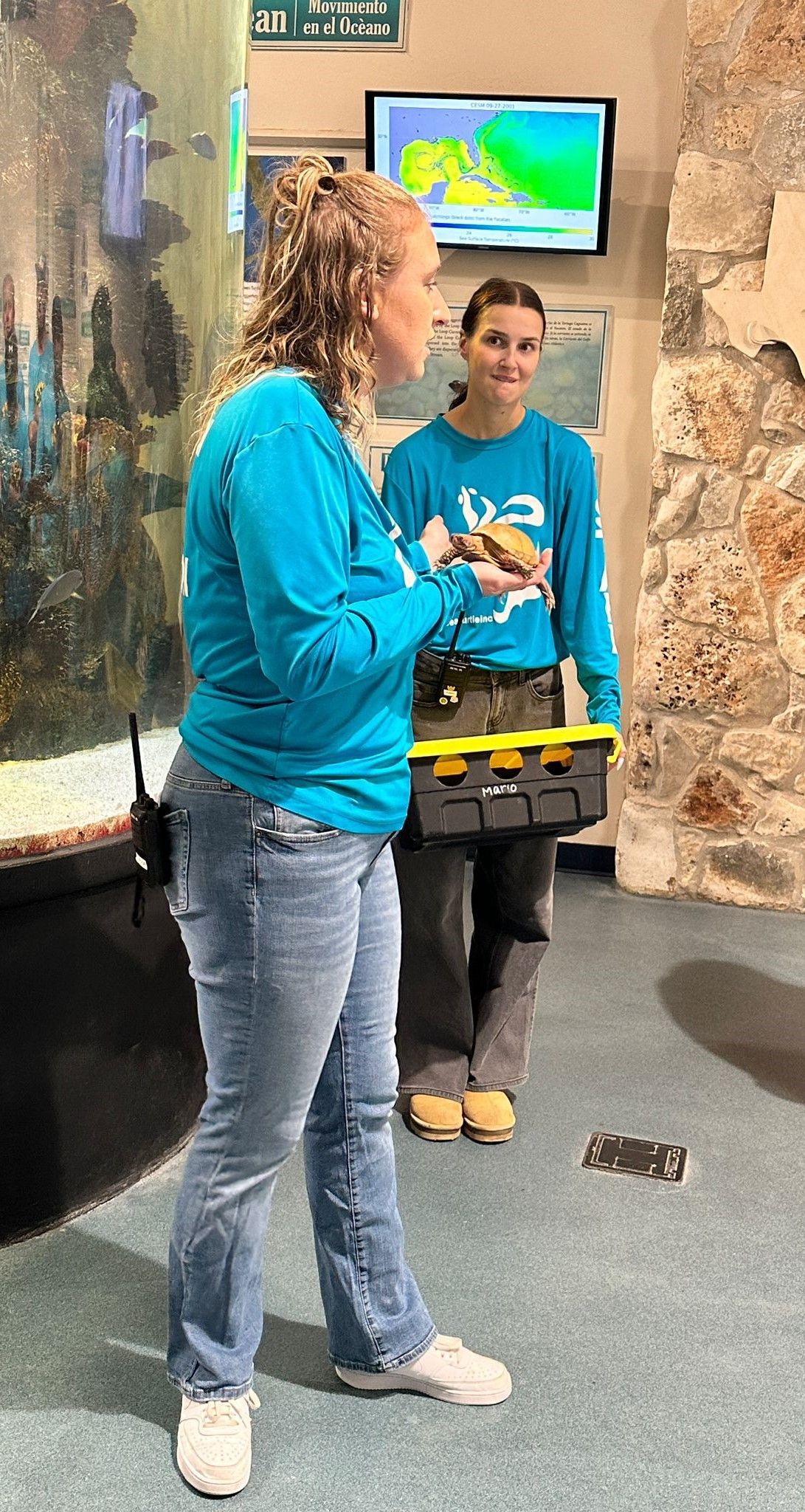 Two women in blue shirts are standing next to each other in a room.