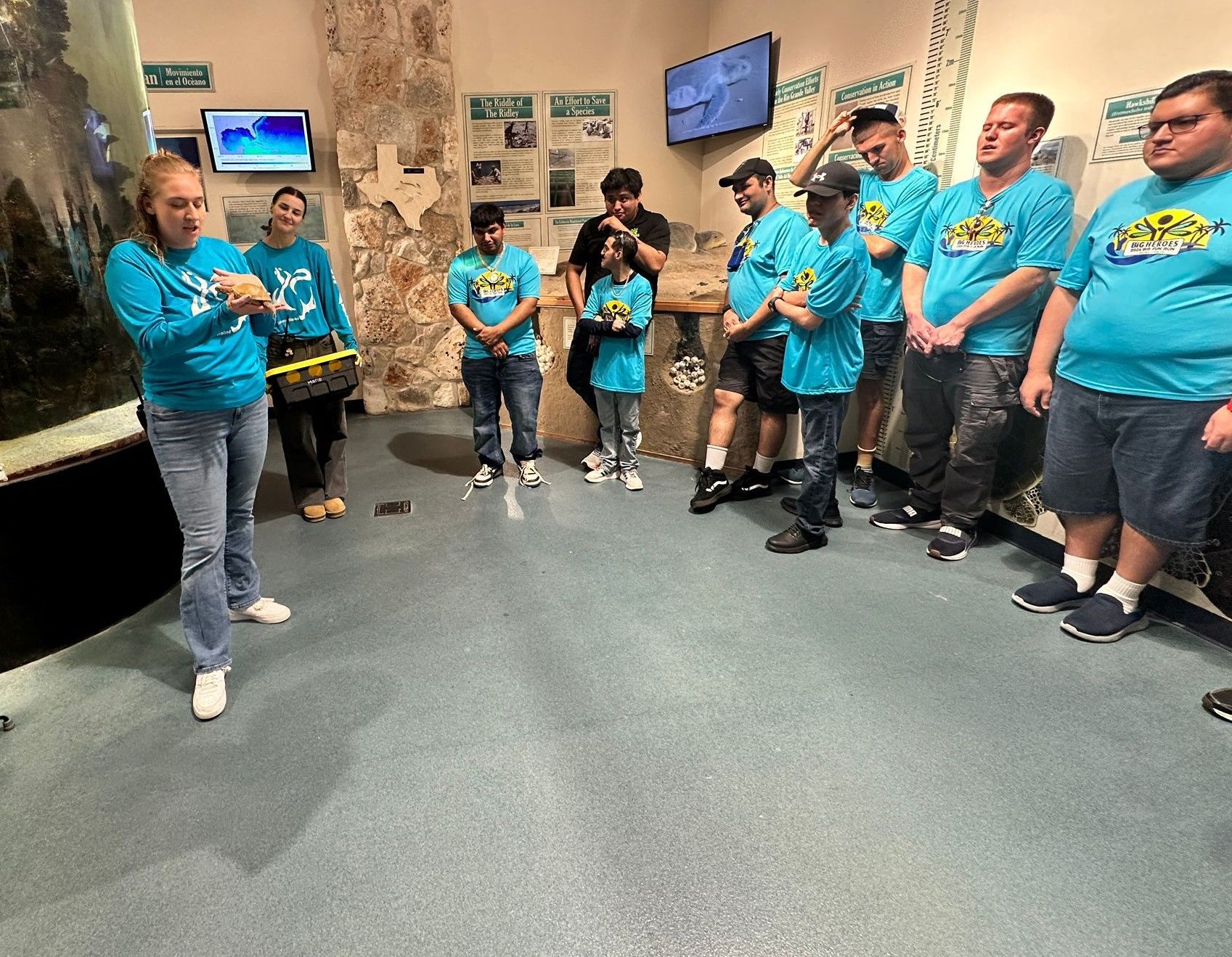 A group of people in blue shirts are standing in a room.