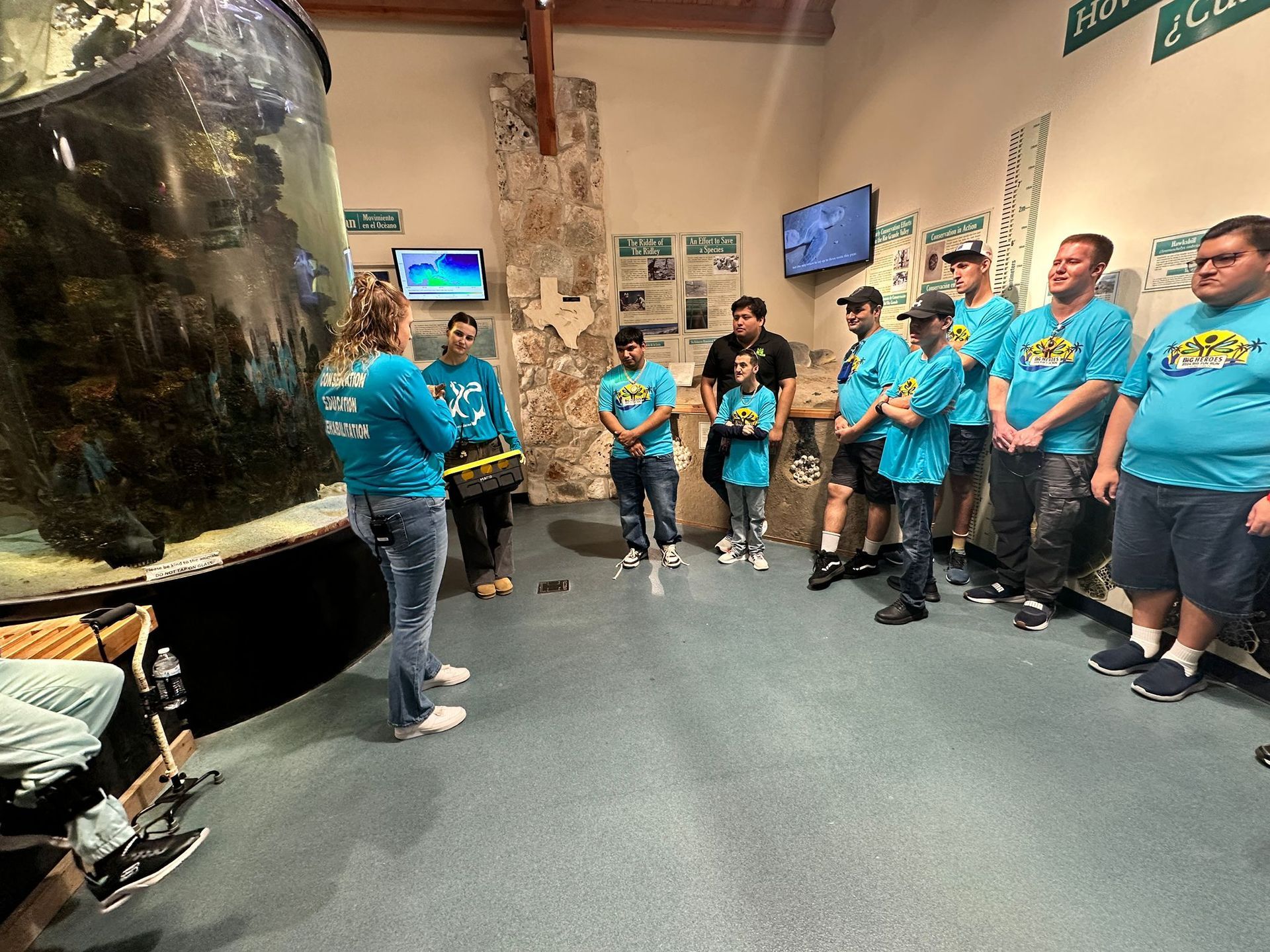 A group of people in blue shirts are standing in front of an aquarium.