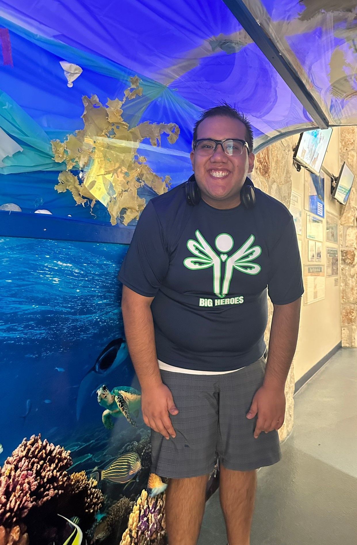A man wearing glasses and a black shirt is standing in front of an aquarium.