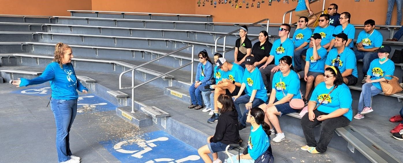 A woman is standing in front of a group of people sitting on bleachers.