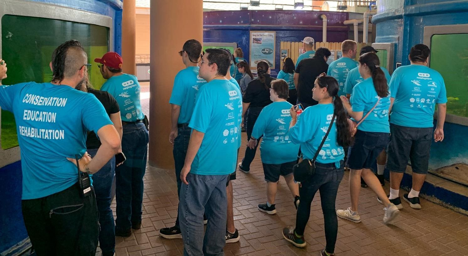 A group of people wearing blue shirts are standing in a room.