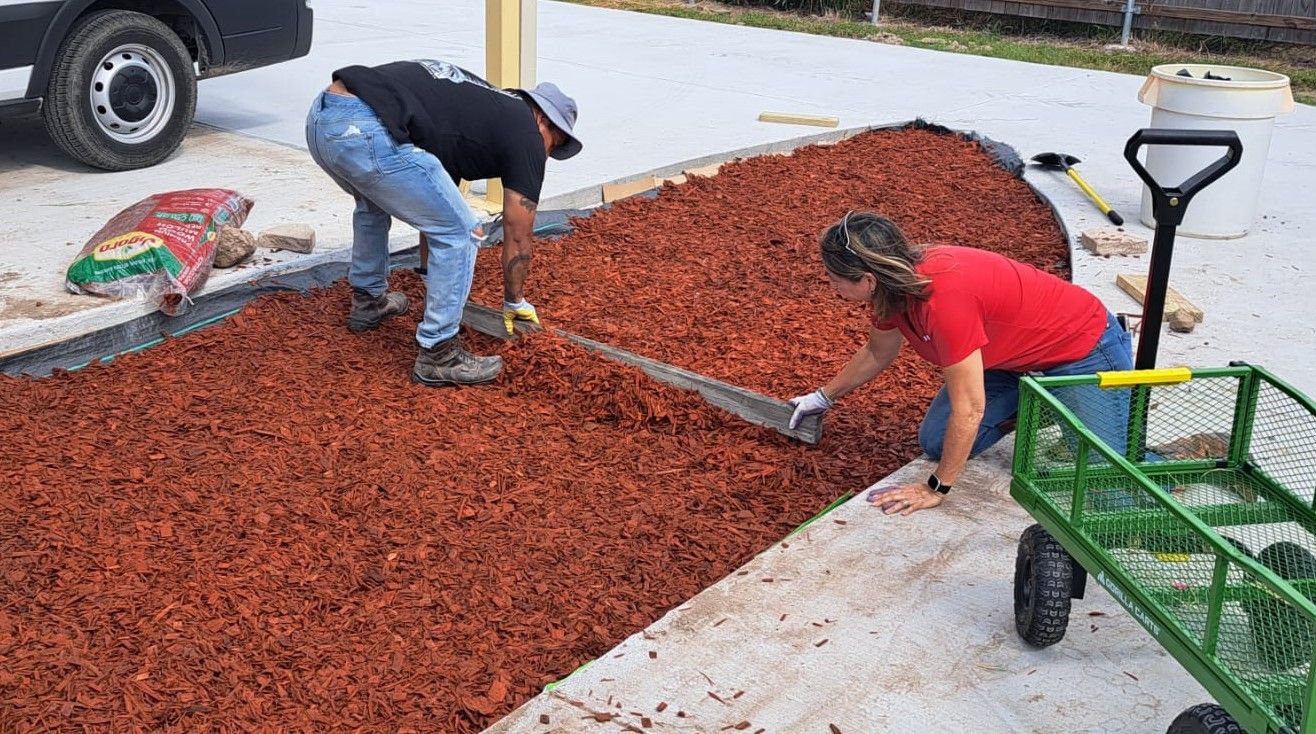 A man and a woman are laying mulch on a sidewalk.