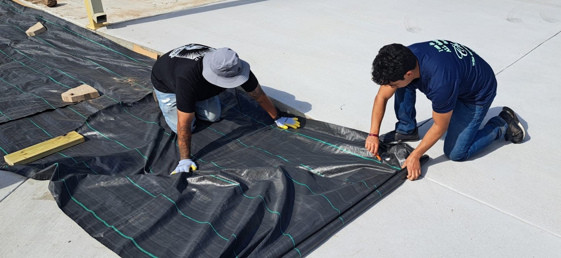 Two men are measuring a piece of black tarp on the ground.
