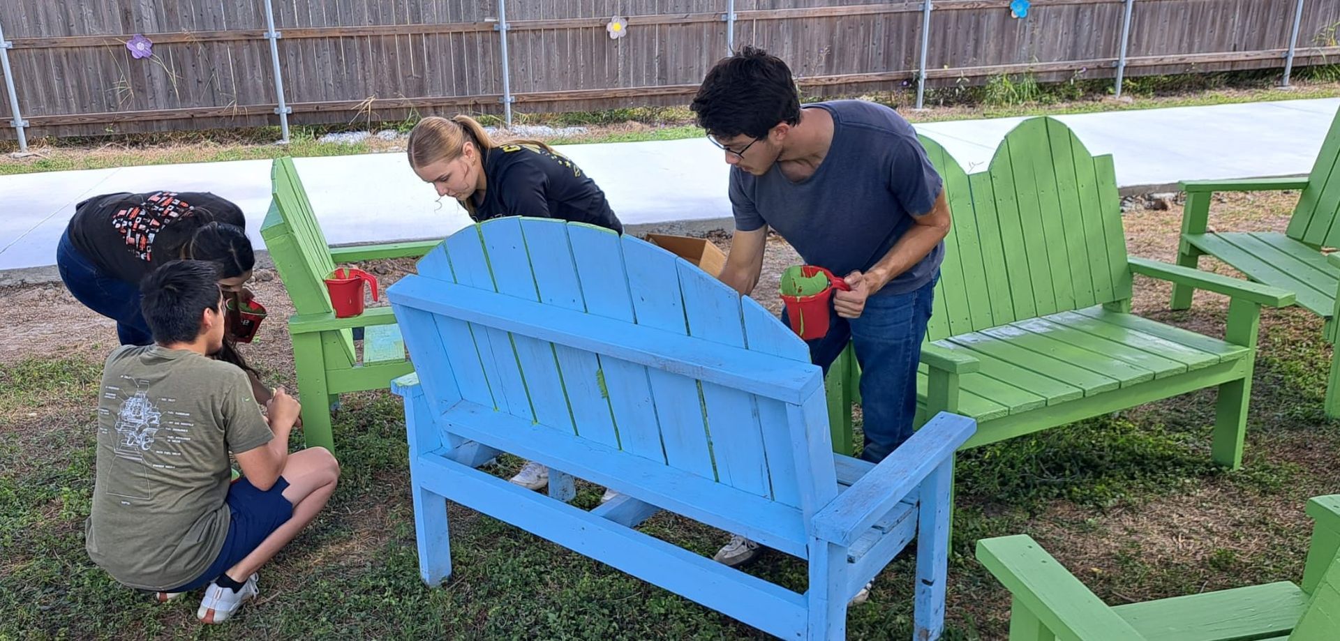 A group of people are working on a blue and green bench.