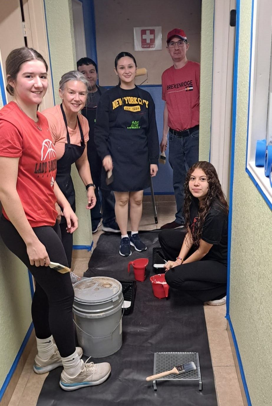 A group of people are standing in a hallway painting a wall.