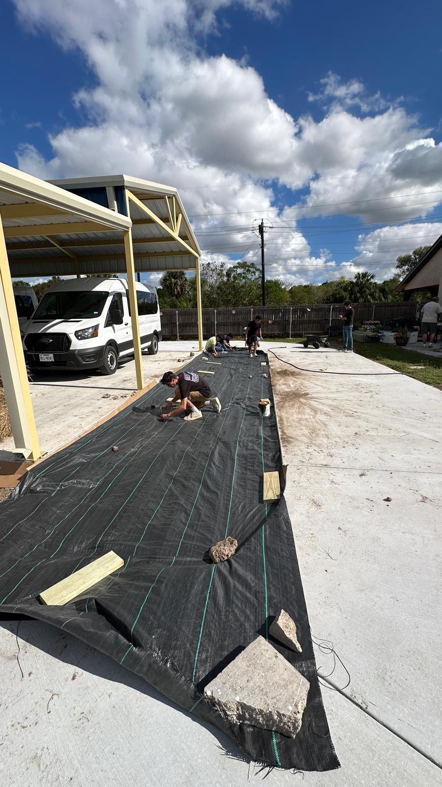 A person is laying on a black tarp in a parking lot.