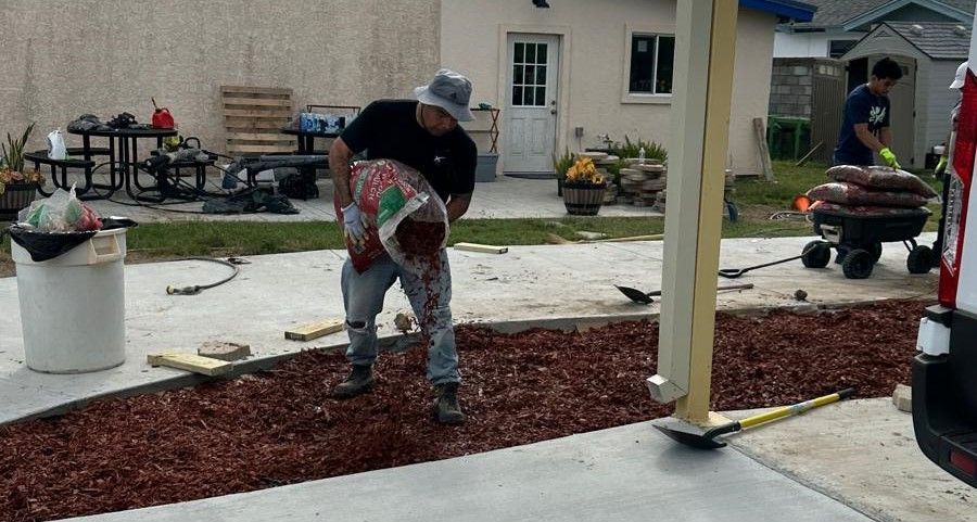 A man is pouring a bag of mulch into a driveway.