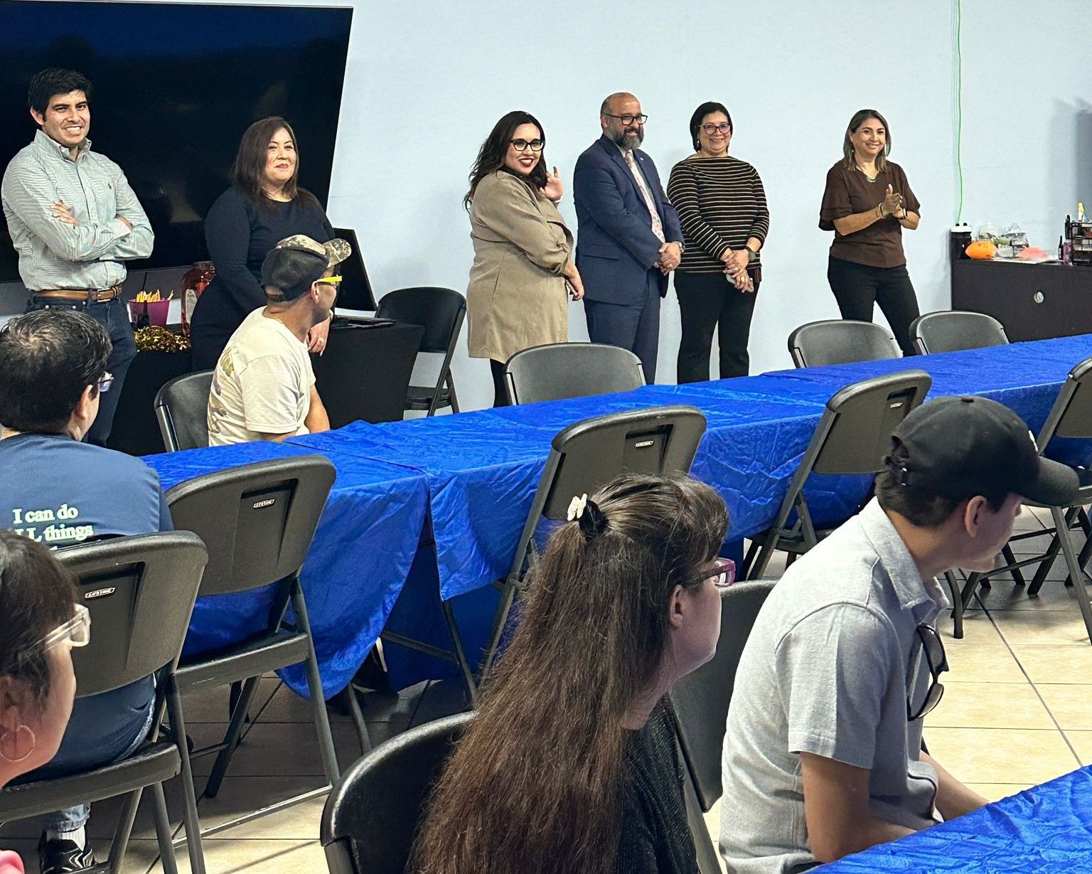 A group of people are sitting at tables with blue tables cloths.