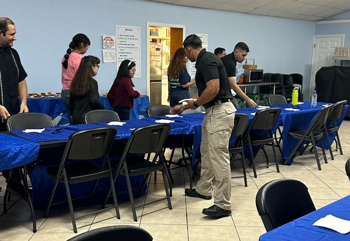A group of people are sitting at tables in a room with blue tables and chairs.