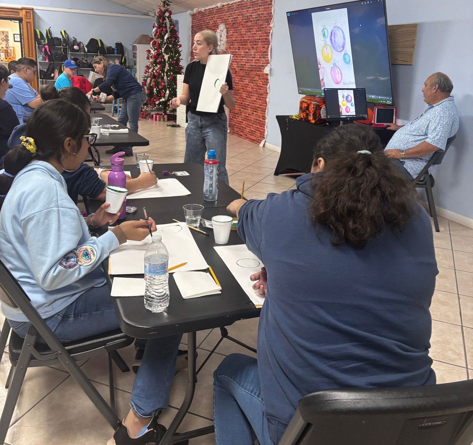A group of people are sitting at tables in a room with a christmas tree in the background