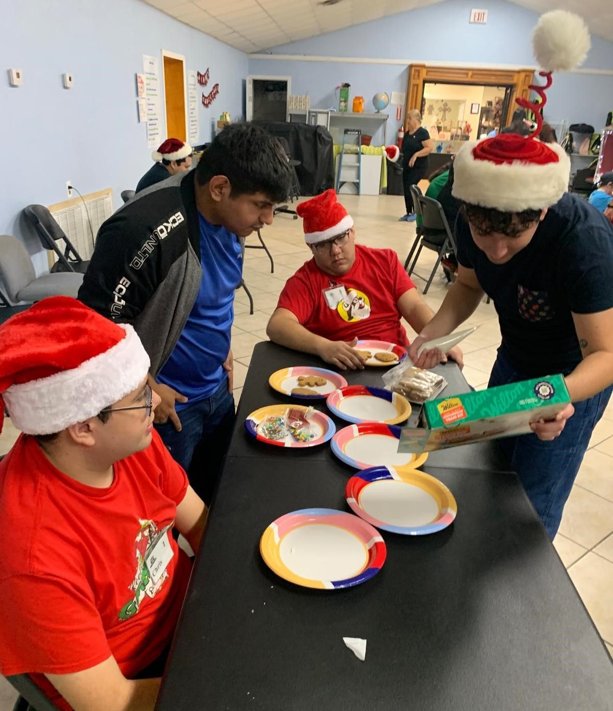 A group of men wearing santa hats are sitting at a table with plates of food
