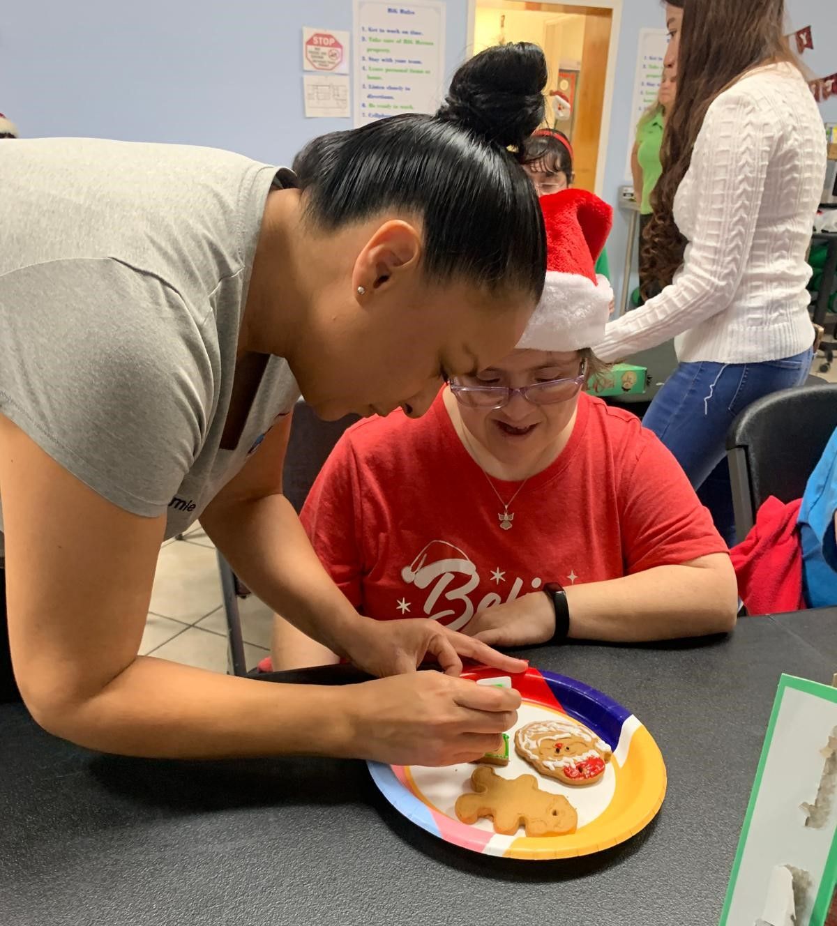 A woman in a santa hat is helping a child with a plate of cookies